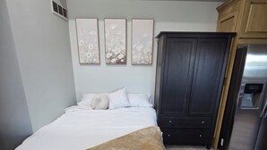 A bedroom with a bed, a dark wardrobe, and a refrigerator.