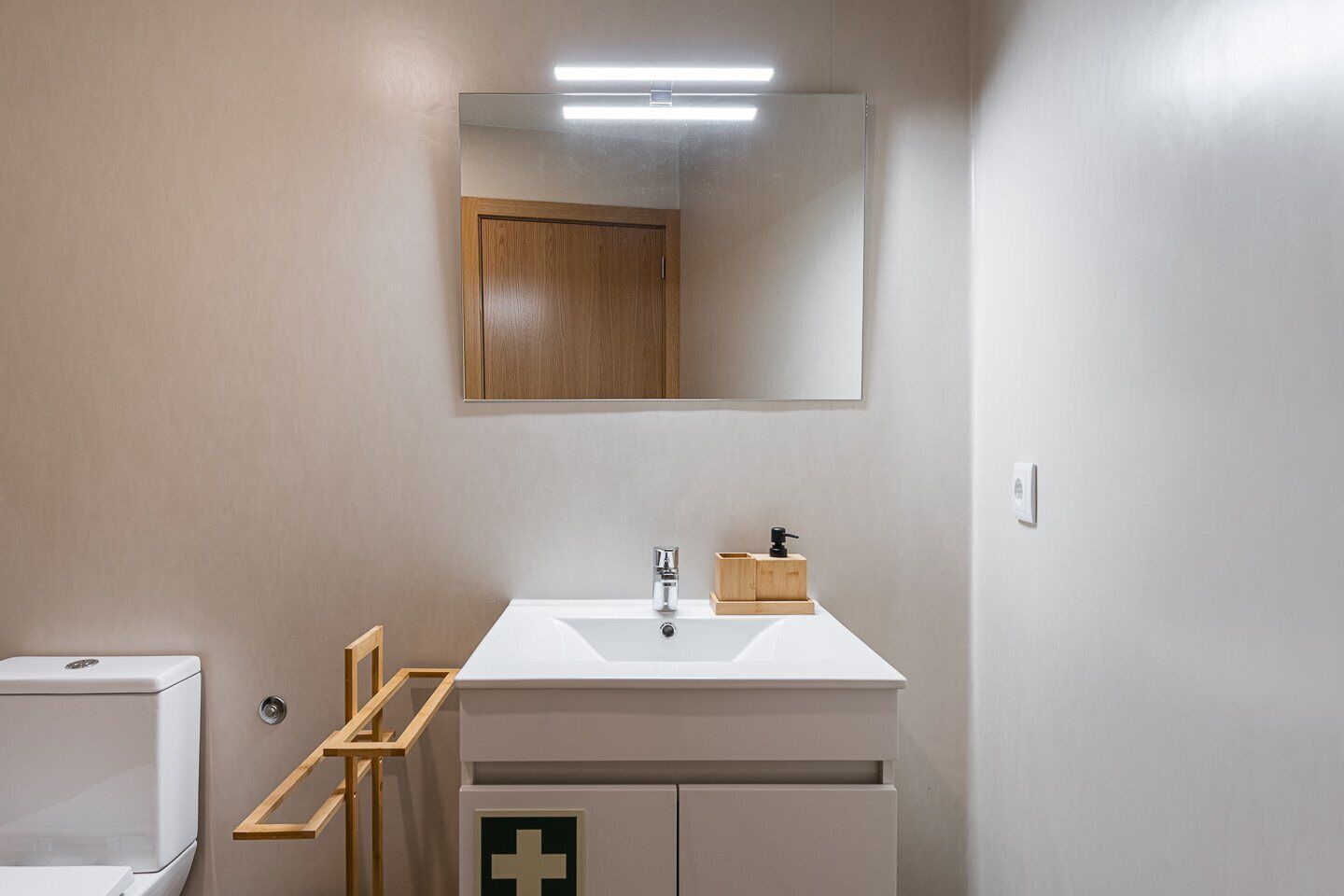 A bathroom with a white sink, wooden cabinet, and a mirror above the sink.