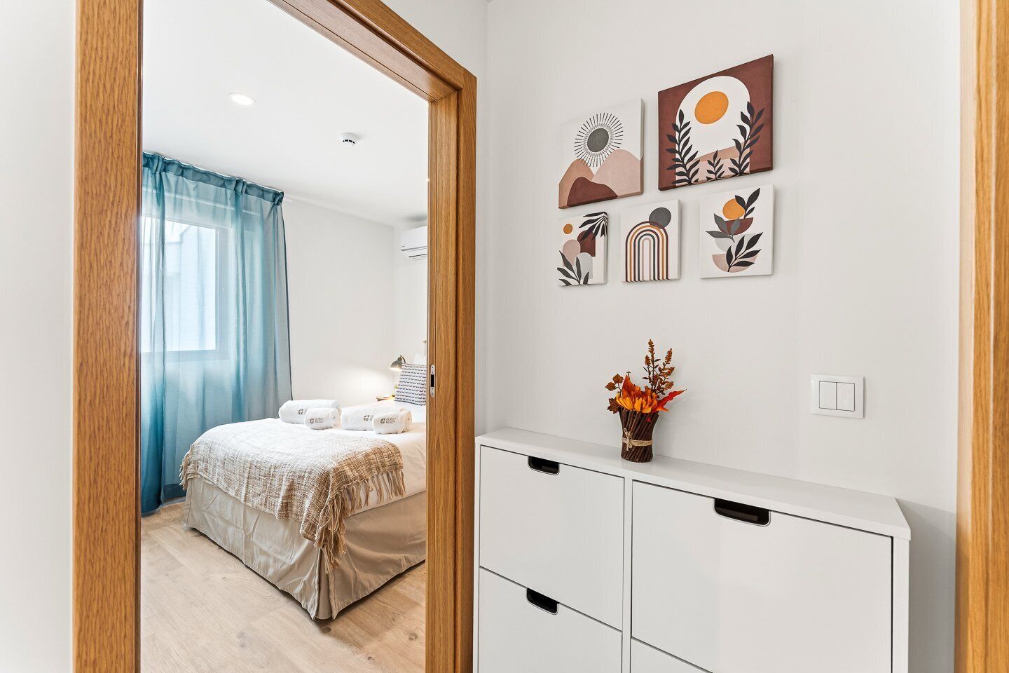 A bedroom with a bed, a bedside table with a vase of flowers, and wall art.