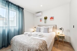 Ein ordentlich eingerichtetes Hotelzimmer mit Bett, Nachttischen, einer Lampe und einem Fenster mit Vorhängen.