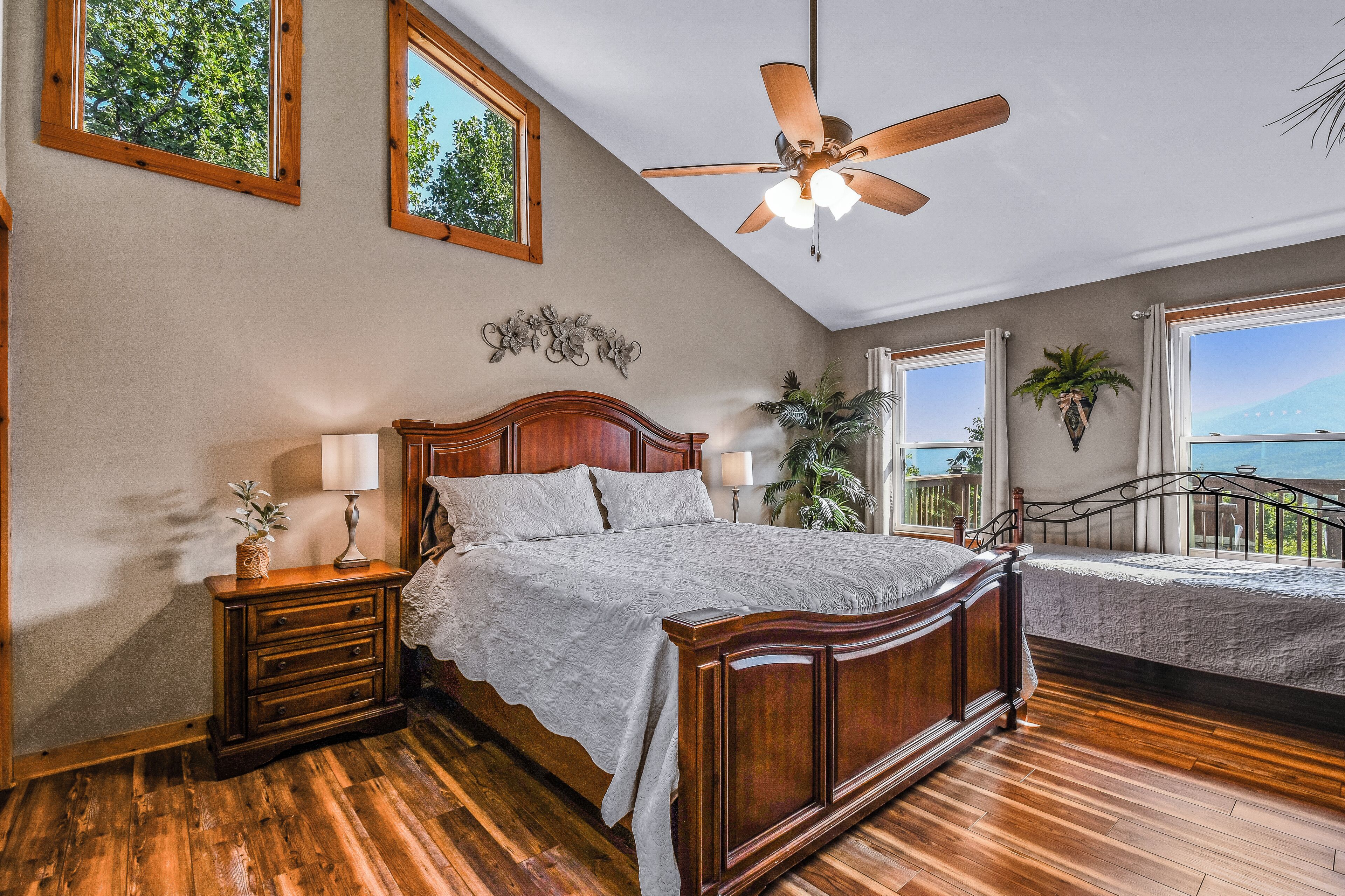 A bedroom with a wooden bed, a nightstand, a ceiling fan, and large windows with a view.