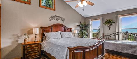 A bedroom with a wooden bed, a nightstand, a ceiling fan, and large windows with a view.