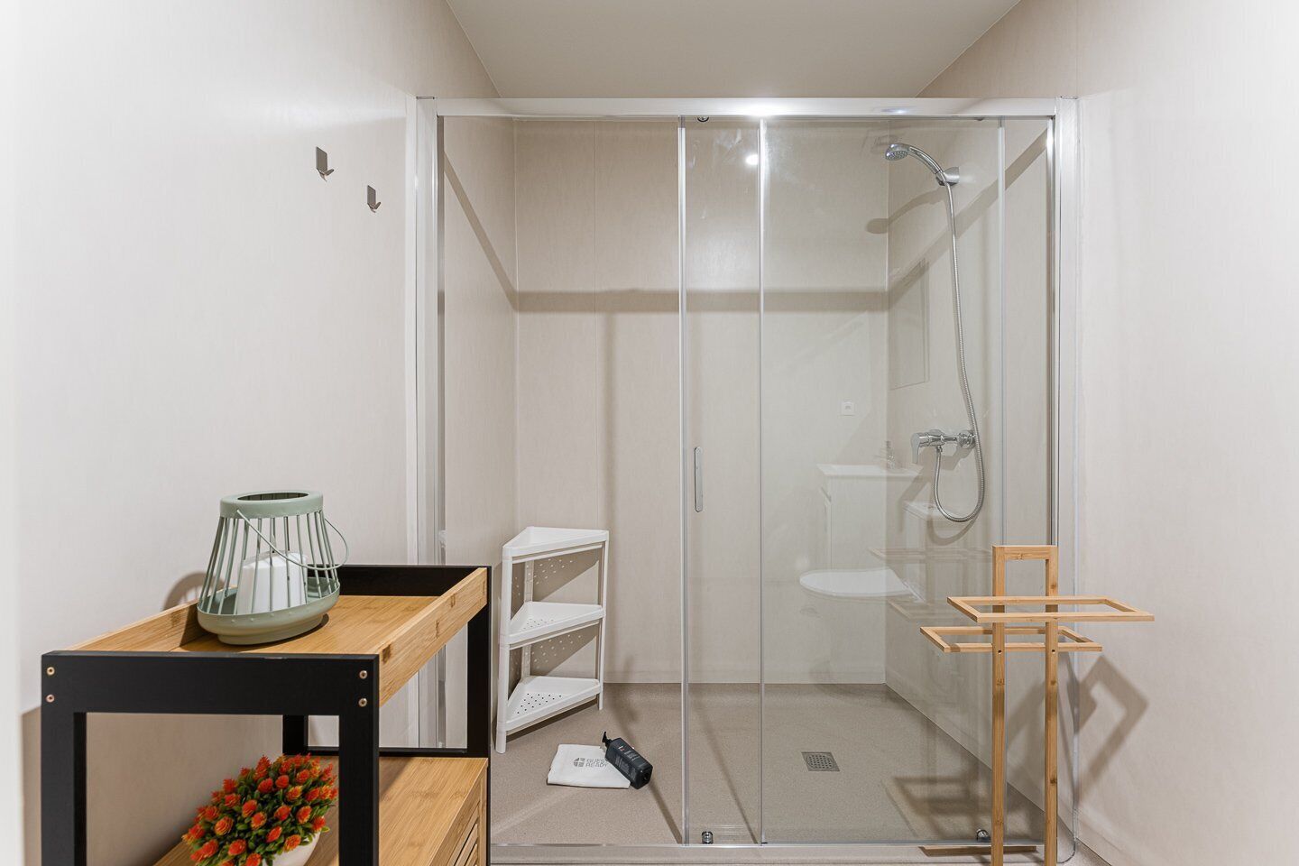 A modern bathroom with a glass-enclosed shower, a wooden shelf with a decorative item, and a white sink.