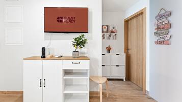 A hotel room with a white cabinet, a television, a small table with a plant, and a wooden door.