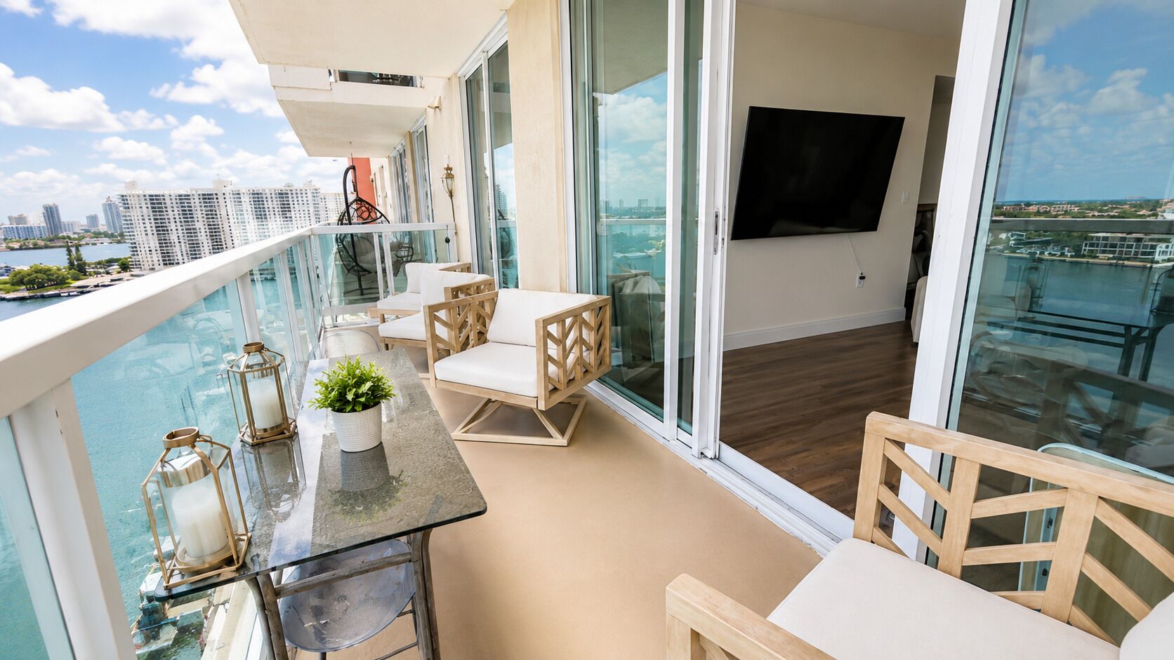 A balcony with a glass railing, a flat-screen TV mounted on the wall, and a view of a cityscape.
