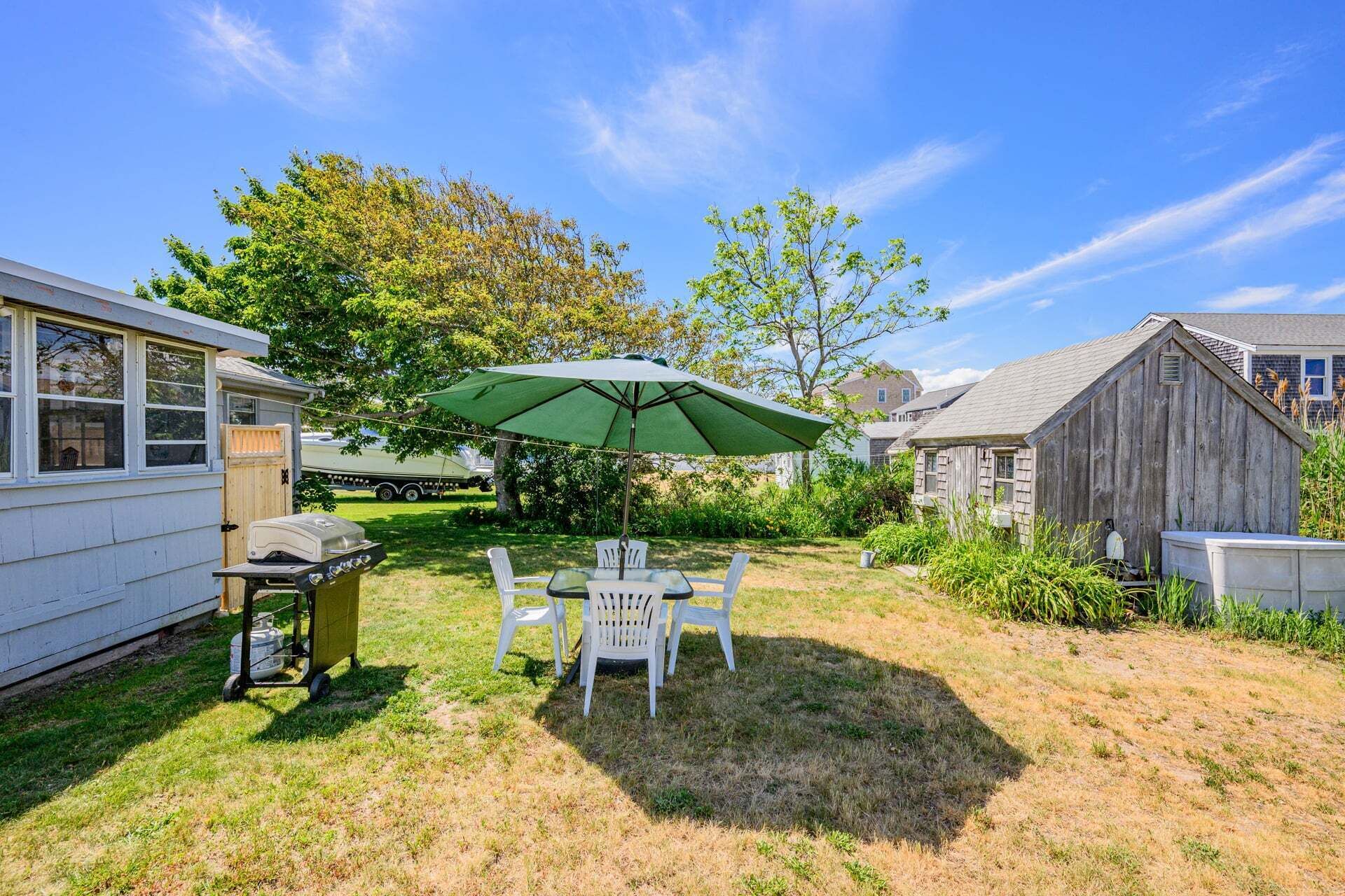 A backyard with a table and chairs under a green umbrella, a grill, and a wooden shed.