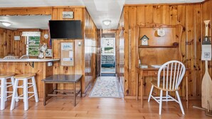 Interior de una cabaña de madera con comedor, televisor y una pequeña cocina.