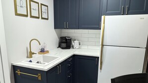 A compact kitchen with dark blue cabinets, a white refrigerator, a coffee maker, and a sink with gold handles. -     Island Escape | Cozy 2BR Suite Steps from the Shore (Parksville)