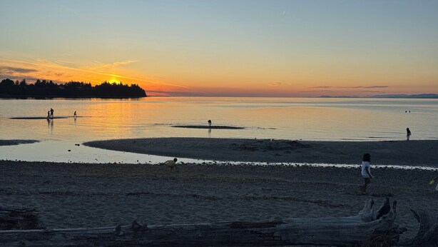 A beach with calm water, a sunset, and a few people walking. -     Island Escape | Cozy 2BR Suite Steps from the Shore (Parksville)