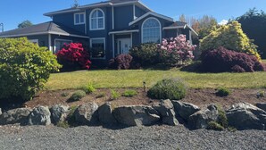 A two-story house with a large front porch, a garage, and a well-maintained lawn. -     Island Escape | Cozy 2BR Suite Steps from the Shore (Parksville)