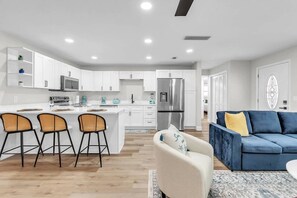 Une cuisine moderne avec des meubles blancs, un îlot central et un coin repas doté de chaises en osier.
