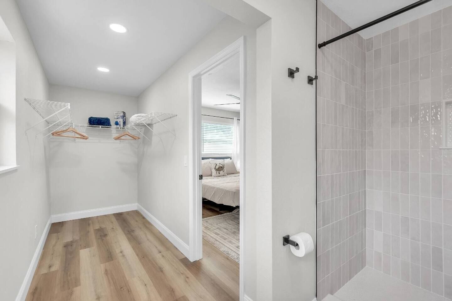Un pasillo con piso de madera, una cabina de ducha de vidrio y una cama en la habitación contigua.