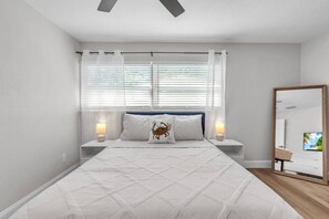 Ein Schlafzimmer mit einem Bett, zwei Nachttischlampen, einem großen Spiegel und einem Fernseher an der Wand.