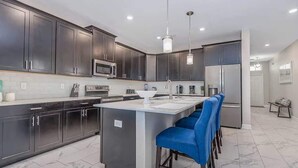 A modern kitchen with dark cabinets, a central island, bar stools, and stainless steel appliances. - Cozy 6BR Home,Sleeps 16,Near Disney & Universal FL (Four Corners)