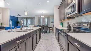 A modern kitchen with dark cabinets, a large island, and a built-in microwave. - Cozy 6BR Home,Sleeps 16,Near Disney & Universal FL (Four Corners)