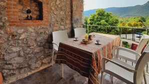 Un mur de pierre, une table recouverte d’une nappe à motifs et une vue sur la verdure et les collines.