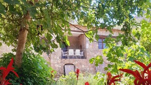 Un bâtiment en pierre doté d’un balcon, entouré d’une végétation luxuriante et de fleurs rouges.