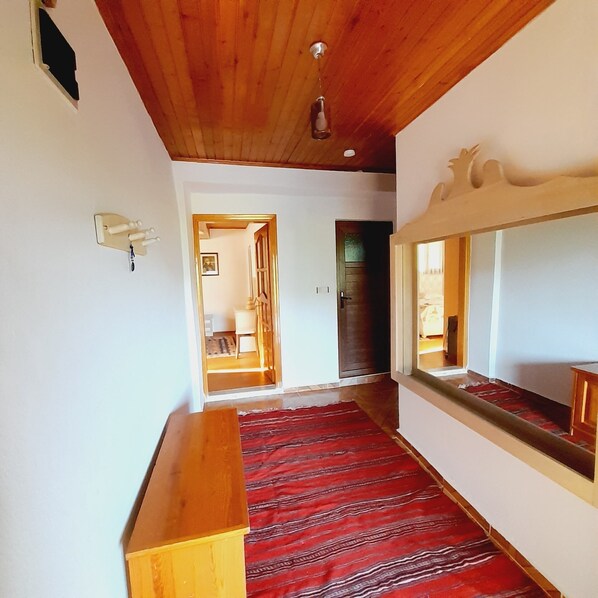 A hallway with a wooden bench, a red patterned carpet, and a large mirror on the right.