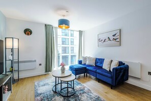 A modern living room with a blue sofa, a round table, and a large window with curtains. - Central Stylish And Spacious 2BDR Flat (Greater Manchester)