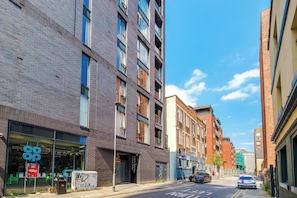 A street view with modern buildings, a clear sky, and a car parked on the side. - Central Stylish And Spacious 2BDR Flat (Greater Manchester)