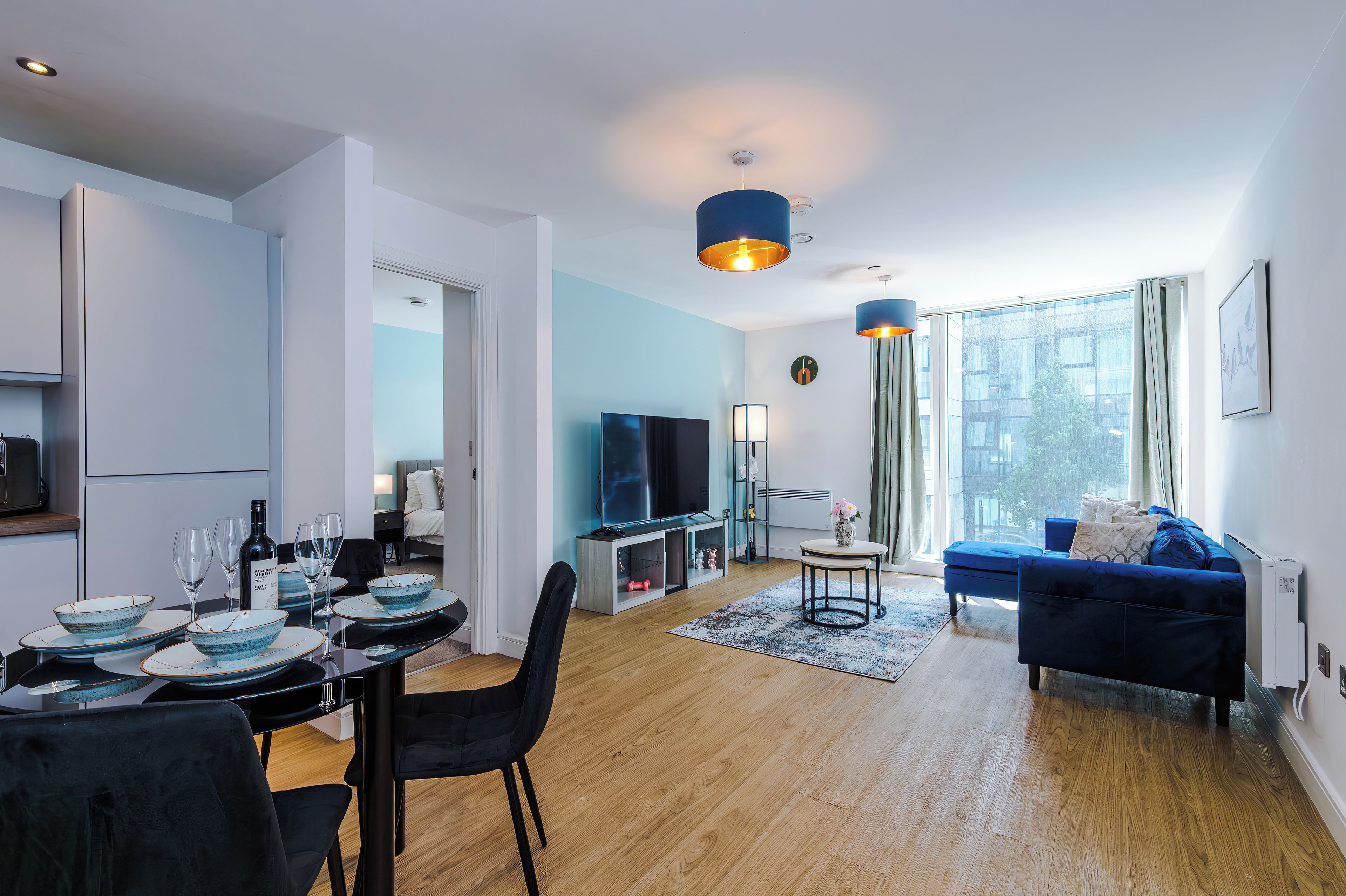 Un salon moderne comprenant un coin repas, un canapé, un téléviseur et une grande fenêtre.