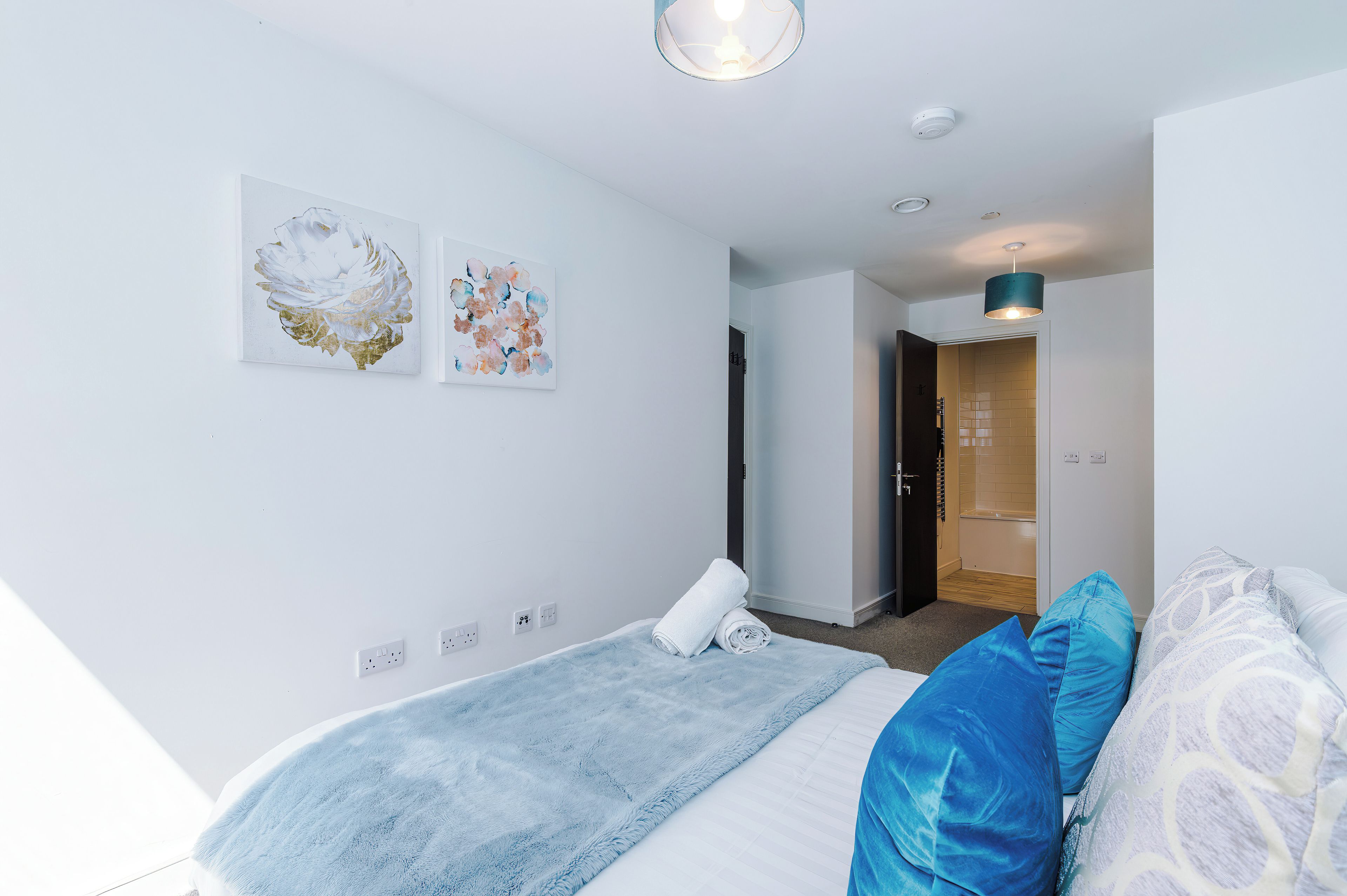 A bedroom with a bed, a towel, a blue and white patterned pillow, and two wall-mounted artworks.