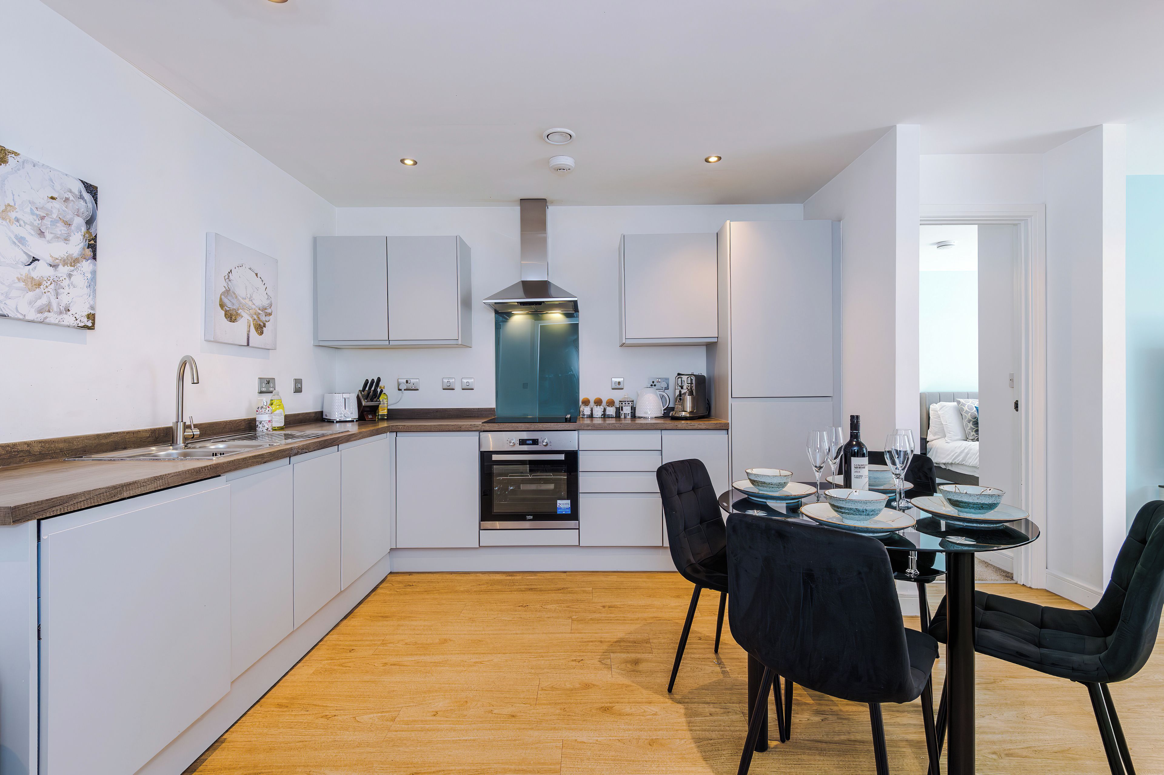 A modern kitchen with white cabinetry, a built-in oven, and a dining area with a table set for two.
