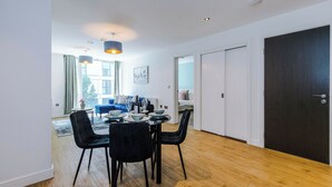 Een moderne eethoek met een houten vloer, zwarte stoelen, een ronde tafel en hanglampen.