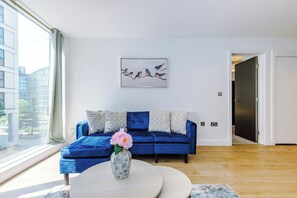 A modern living room with a blue sofa, a white vase with flowers, and a painting of birds on the wall. - Central Stylish And Spacious 2BDR Flat (Greater Manchester)
