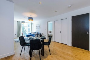 A modern dining area with a wooden floor, black chairs, a round table, and pendant lighting. - Central Stylish And Spacious 2BDR Flat (Greater Manchester)