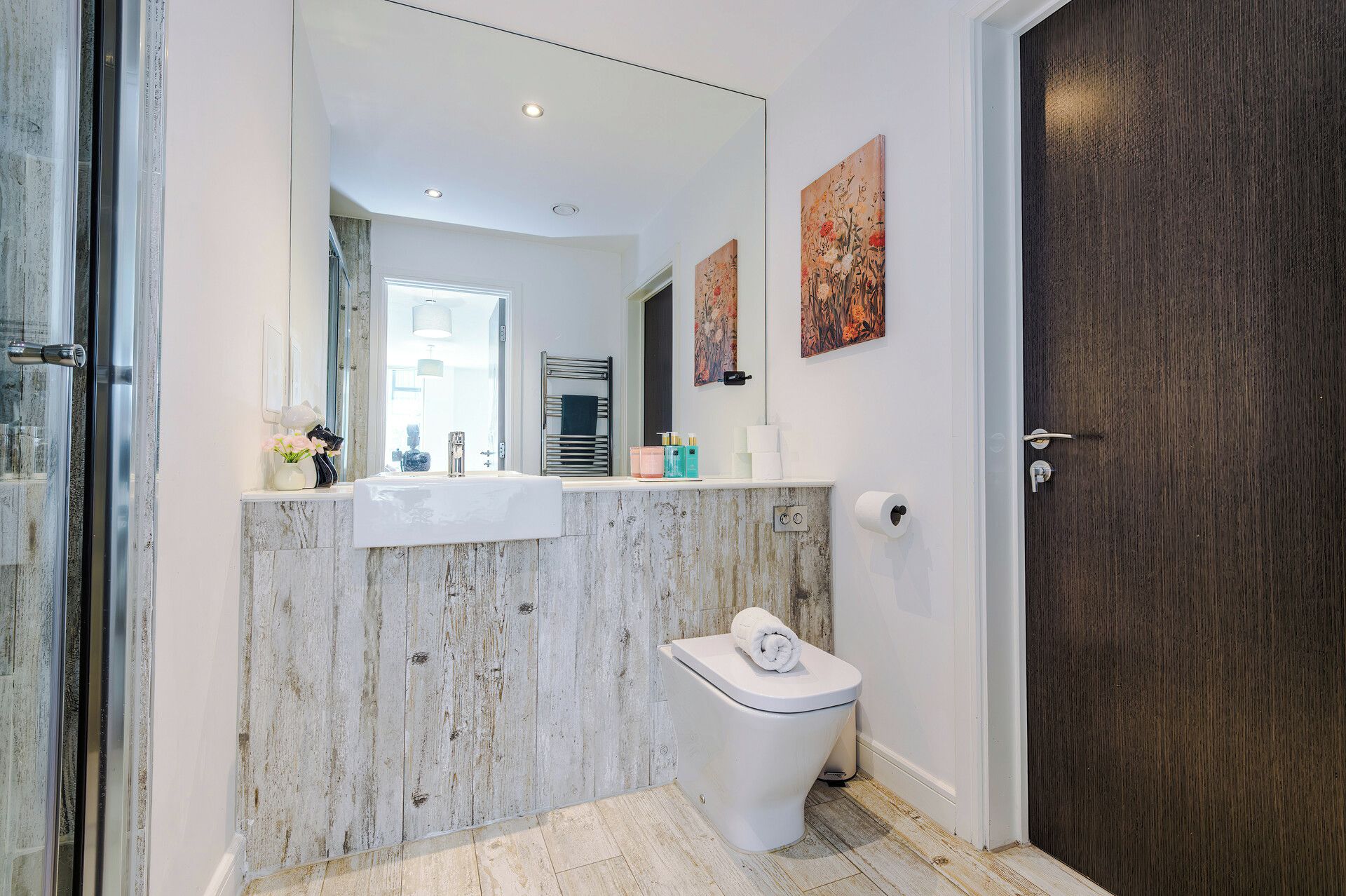 Un baño con un lavabo blanco, un inodoro, un espejo y una puerta de madera oscura.