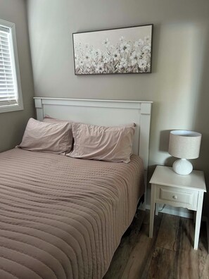 A bedroom with a bed, a nightstand, a lamp, and a wall-mounted artwork.