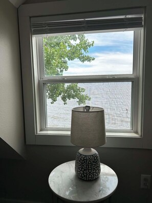 A room with a window, a lamp on a table, and a view of trees and sky.