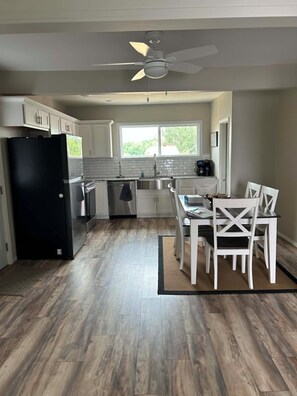 A kitchen with a black refrigerator, white cabinets, a dining table with white chairs, and a ceiling fan.
