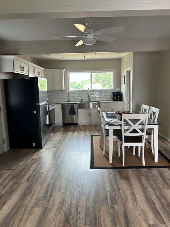 A kitchen with a black refrigerator, white cabinets, a dining table with white chairs, and a ceiling fan.