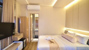 Habitación de hotel con cama, televisor, escritorio, espejo y aire acondicionado.