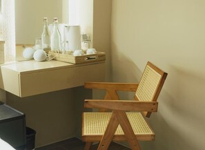 Una silla de madera con asiento tejido en una habitación con pared color beige y una encimera con diversos objetos.