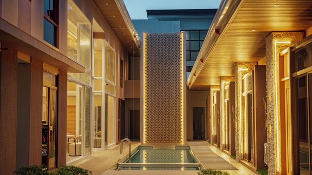 Un pasillo moderno de hotel con piscina central, puertas de vidrio y pared con diseño.