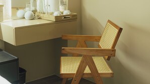 Una silla de madera con asiento y respaldo de mimbre, un escritorio beige con una bandeja tejida, y varias botellas de vidrio y recipientes blancos sobre el escritorio.