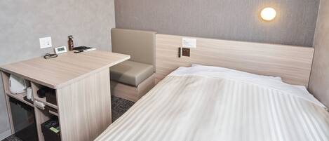 A hotel room with a bed, a desk with a chair, a small sofa, and a wall-mounted light.