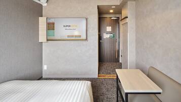 Habitación de hotel con cama, una mesita, un panel informativo en la pared y una puerta que da a otra habitación.