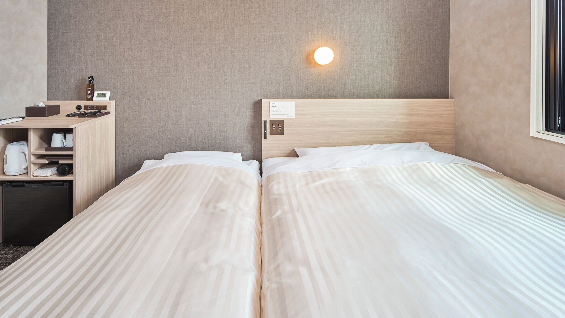 Ein Hotelzimmer mit zwei Betten, einem Schreibtisch mit Kaffeemaschine, einem Nachttisch und einer Wandleuchte.
