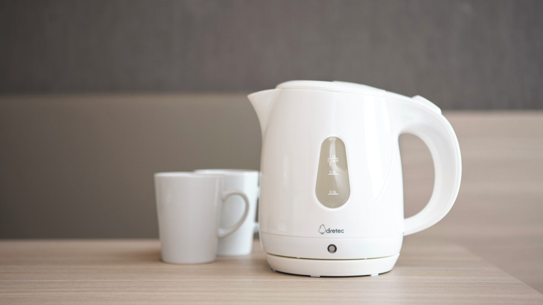 A white electric kettle with a digital display and a cup on a wooden surface.