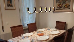 Ein Esszimmer mit Tisch für vier Personen, umgeben von Korbstühlen, einer gemusterten Tischdecke und einer Kronleuchter.