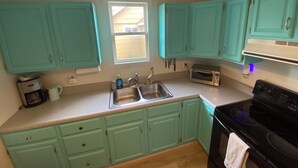 Une cuisine avec des armoires de couleur turquoise, un évier à deux bacs, un four à micro-ondes et une cuisinière.