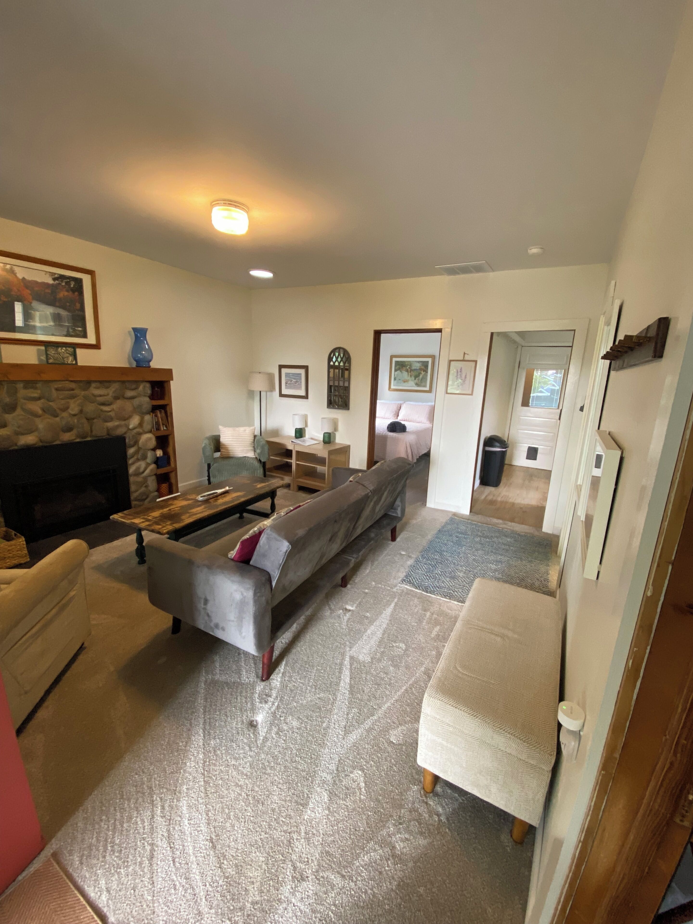Una sala de estar con chimenea, sofá y televisor. Se ve un pasillo que conduce a otra habitación.