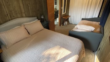 A bedroom with a large bed, a smaller bed, a wooden wall, a mirror, and a window with curtains.