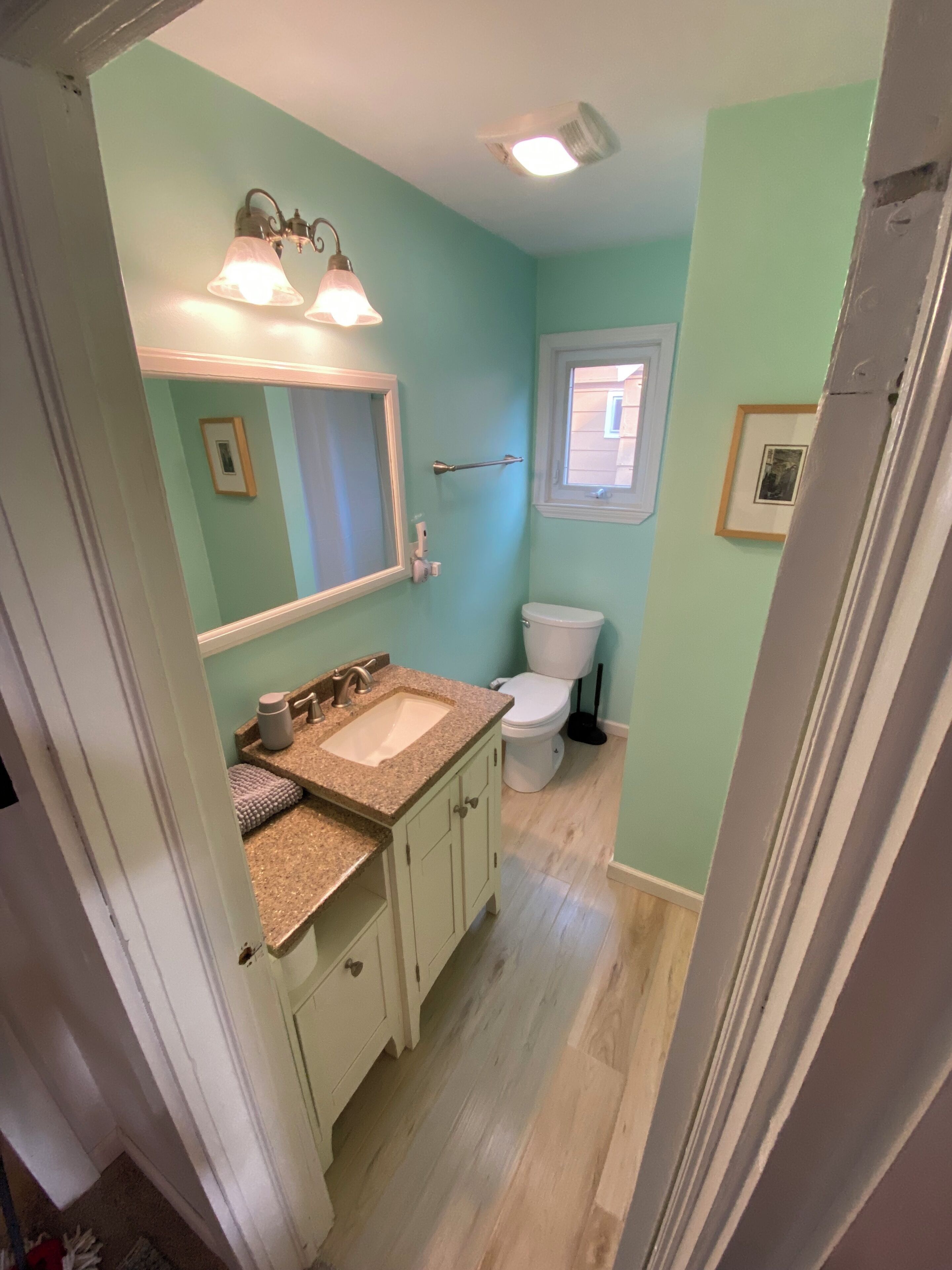 Une salle de bain comprenant des toilettes, un lavabo et un meuble-lavabo. Il y a une fenêtre au-dessus des toilettes et un miroir au-dessus du lavabo.
