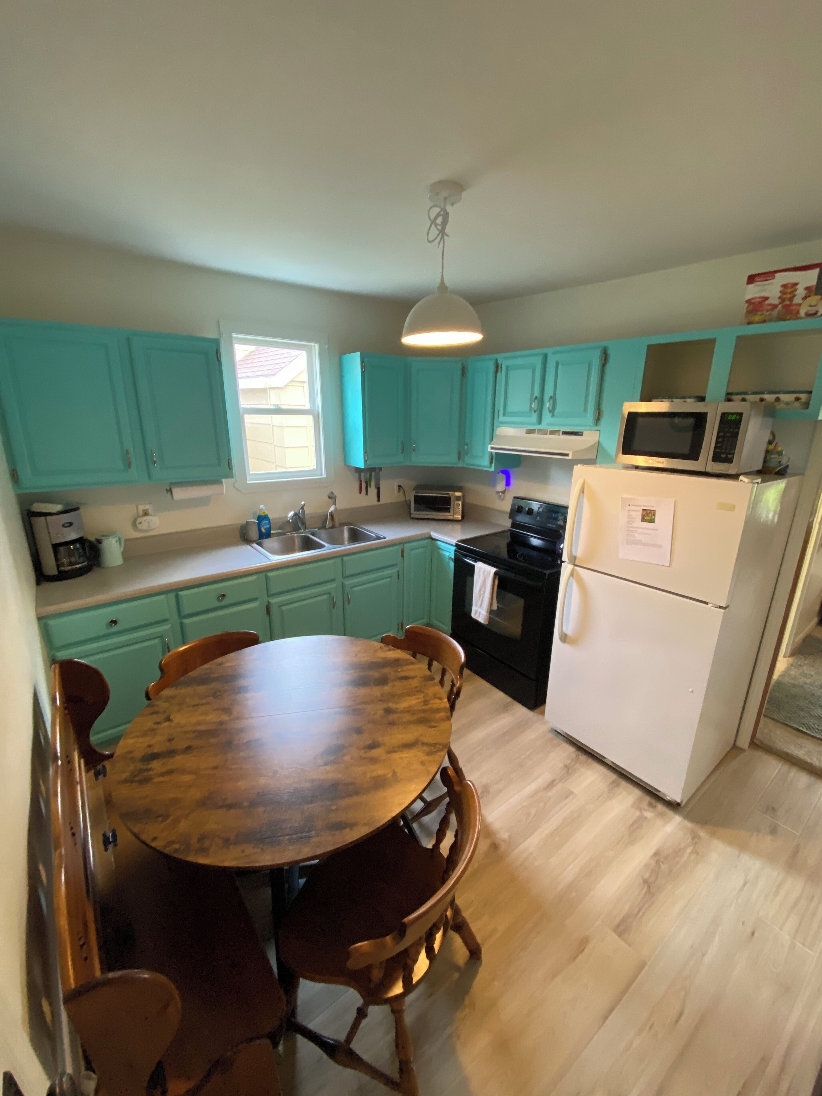A kitchen with teal cabinets, a wooden dining table, and a white refrigerator.