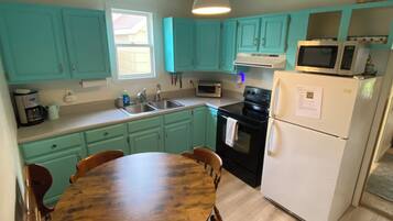 A kitchen with teal cabinets, a wooden dining table, and a white refrigerator.